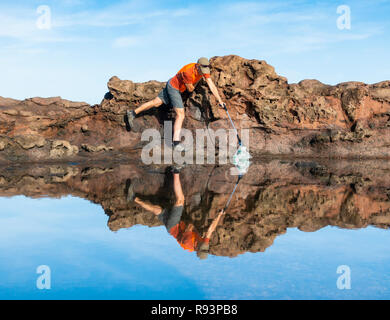 Ein Plogger/Jogger sammelt Plastikmüll am Strand während seines morgendlichen Lauf Stockfoto