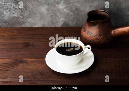 Kaffee in weiße Tasse und Lehm cezve auf hölzernen Hintergrund Stockfoto