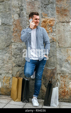 Junger Mann mit Einkaufstüten und Mobile Stockfoto