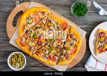 Leckere Pizza mit Pilzen, Huhn, Peperoni, Oliven, Mais in Stücke geschnitten auf einer hölzernen Fach. Die Ansicht von oben Stockfoto