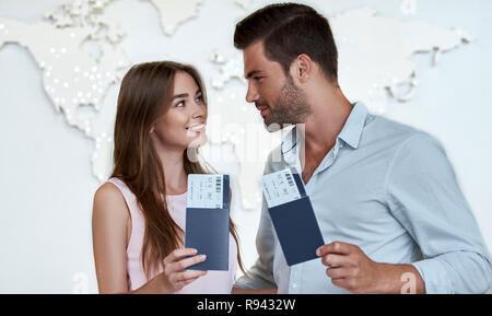 Portrait von freudiger froh Paar hält Reisepass mit fliegenden Karten in den Händen zeigt mit dem Zeigefinger zu jedem anderen Suchen auf der Karte Hintergrund Stockfoto