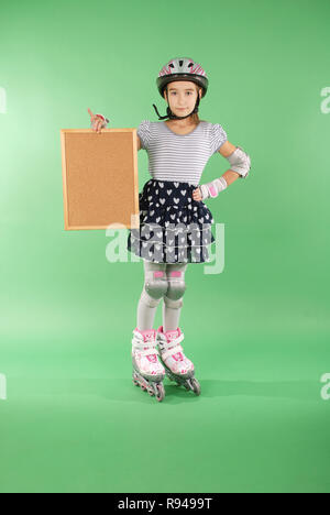 Hübsches Mädchen mit rollerskates gegen grüne Hintergrund isoliert. Sie hält einen hölzernen Rahmen, in dem Sie Text schreiben können. Stockfoto