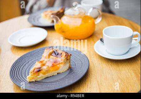 Orange pfirsich Gelee Kuchen auf Holz- Hintergrund. Stück pfirsich Gelee Kuchen aus ganze Torte Torte und einer Tasse Meer geschnitten - Sanddorn Tee. Frühstück im St Stockfoto