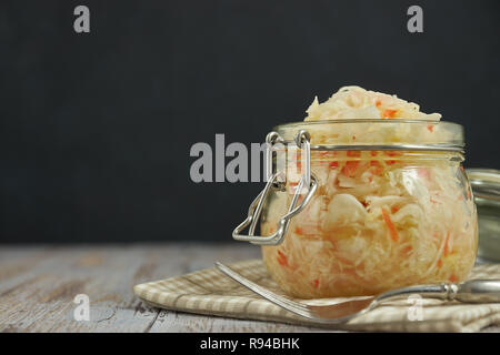 Ein Glas von Sauerkraut und Karotten im eigenen Saft mit Gewürzen auf leichte, weiße Holztisch, ein vertikaler Art von Kohl in einem jar. traditionellen Home-m Stockfoto