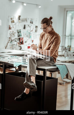 Junge Designer aus der Mode Schule mit einer Uhr auf der Hand sitzen auf einem Tisch Stockfoto