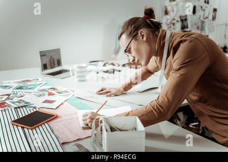 Hübscher junger Designer aus einer Modeschule in Brillen notieren Messungen Stockfoto