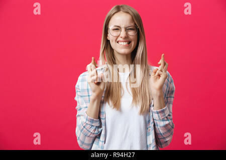 Portrait von Wunschdenken junge Frau in Freizeitkleidung mit blond gefärbten Haaren, überschreiten ihre Finger, biss sich auf die Unterlippe, nervös vor dem wichtigen Ereignis. Körpersprache. Stockfoto