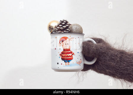 Thema Weihnachten. in der Hand, eine Tasse mit einem Schwein und Weihnachtskugeln. Bokeh im Hintergrund. Lichter. Stockfoto