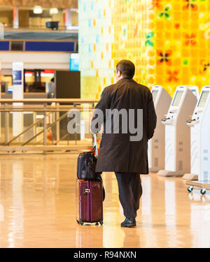 TOKYO, JAPAN - 7 November, 2017: der Mann, der in einen Regenmantel mit einem Koffer am Flughafen. Ansicht von hinten. Mit selektiven Fokus Stockfoto