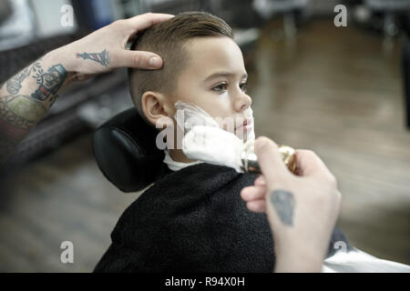 Kinder Friseur Schneiden kleiner Junge vor einem dunklen Hintergrund. Zufriedene cute Vorschüler Boy, die Haare schneiden lassen. Stockfoto