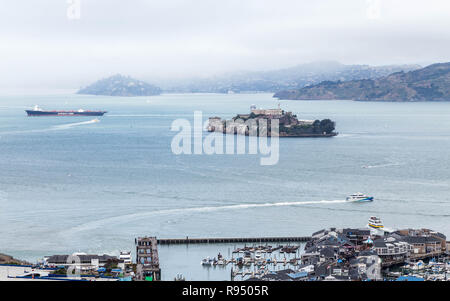 Hochwinkelblick auf Alcatraz Island und Pier 39 in der Bucht von San Francisco mit Booten und einem Tankschiff an einem nebeligen Tag, Kalifornien, USA Stockfoto