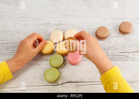 Die Hände des Kindes spielen mit Macarons auf weißem rustikalen Holztisch Stockfoto