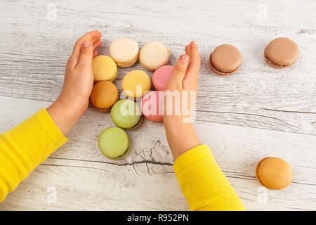 Die Hände des Kindes Blume von Französische macarons auf weissem Holztisch Stockfoto