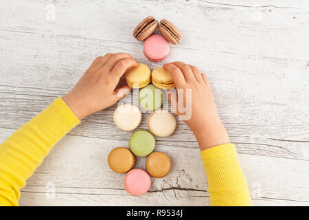 Die Hände des Kindes anordnen Macarons auf weißem rustikalen Holztisch Stockfoto