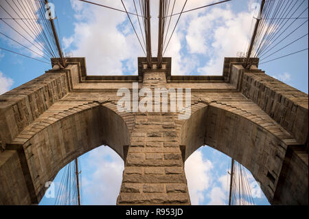 Malerische abstrakte Sicht der Stahlseile und texturierte Steine der ikonischen stone arch Tower der Brooklyn Bridge unter soft Sonnenuntergang Wolken Stockfoto