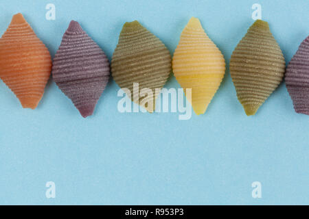 Reihe von bunten Gemüse Pasta Muscheln auf blauem Hintergrund. Nahaufnahme mit Kopie Raum Stockfoto