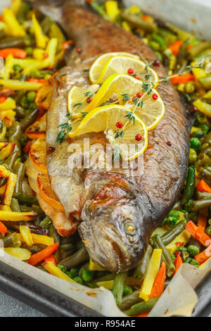 Gebackenen Fisch Forelle mit Gemüse (Kartoffeln, Karotten, Bohnen, grüne Erbsen und Zwiebeln) mit Zitrone, Thymian und rosa Pfeffer. Wildlachs. Lecker er Stockfoto