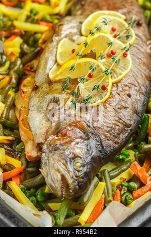 Gebackenen Fisch Forelle mit Gemüse (Kartoffeln, Karotten, Bohnen, grüne Erbsen und Zwiebeln) mit Zitrone, Thymian und rosa Pfeffer. Wildlachs. Lecker er Stockfoto