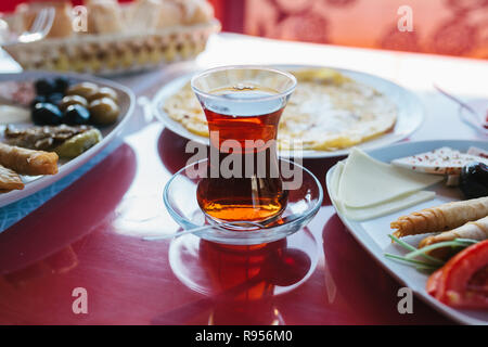 Close-up: Eine heiße Tasse duftenden schwarzen Tee. Zwei Platten mit vegetarischem Essen - frisches Gemüse und Käse, Kuchen und Getränke in Glas Rot, Tabelle Stockfoto