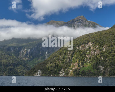 Ein Bruch in den Wolken zeigt rauen Berggipfeln steigen rechts aus dem Wasser entlang Doubtful Sound in Neuseelands Fjordland National Park Stockfoto