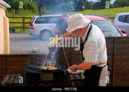 Älterer Mann kochen Fleisch am Grill Stockfoto