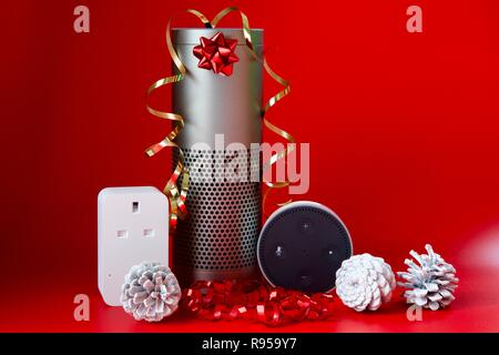 Amazon Echo, Echo Dot und Smart Plug mit Weihnachtsschmuck auf rotem Hintergrund Stockfoto