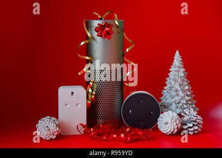Amazon Echo, Echo Dot und Smart Plug mit Weihnachtsschmuck auf rotem Hintergrund Stockfoto