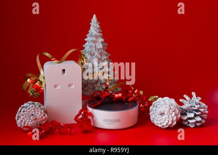 Amazon Echo Dot und Smart Plug mit Weihnachtsschmuck auf rotem Hintergrund Stockfoto