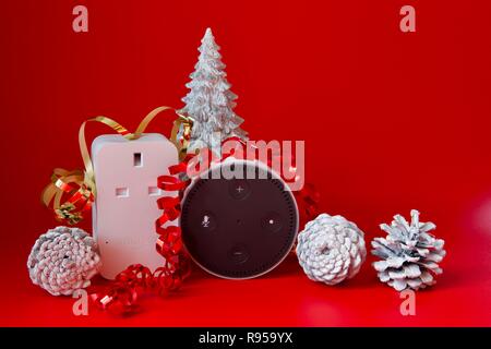 Amazon Echo Dot und Smart Plug mit Weihnachtsschmuck auf rotem Hintergrund Stockfoto