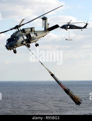 Ein HH-60 UHR Seahawk Hubschrauber, Hubschrauber Anti-Submarine Squadron 11 (HS-11), zieht weg von den Flight Deck der Atom-Flugzeugträger USS Enterprise (CVN 65) mit mehreren leeren Auffüllung Schlingen im Schlepptau, während ein MH-60S Seahawk Hubschrauber, zugeordnet zu den "Bay Räuber" der Hubschrauber Meer Combat Squadron zwei Acht (HSC-28), schwebt in der Nähe der Enterprise fantail. Us Navy Foto des Fotografen Mate 3. Klasse Kristopher Wilson Stockfoto