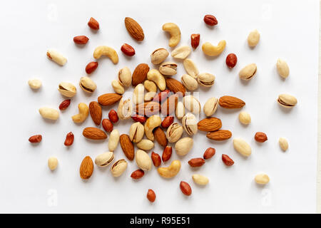Sortierte geröstet und Rohe Nüsse verstreut auf Weiß mit Mandeln, Erdnüsse, Erdnüsse, Pistazien und cashewkerne in einer flachen gesehen lag noch Leben von oben Stockfoto