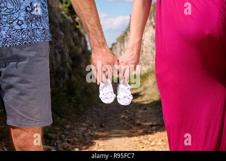 Schwangere Frau und Mann hält Baby Schuhe in den Händen. Zukünftige Mama und Papa, Eltern hält wenig neugeborenen Baby Schuhe. Geburt Erwartung Konzept. Stockfoto