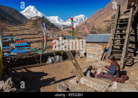 Manaslu (Manasulu), 8. der weltweit höchste Berg in Nepal Himalaya aus dem Dorf der Lho. Tibetischen Frau sitzt das Weben in Vordergrund. Stockfoto