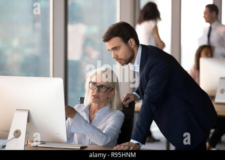 Junge Mitarbeiter hilft im mittleren Alter Kollege lernen Corporate progr Stockfoto