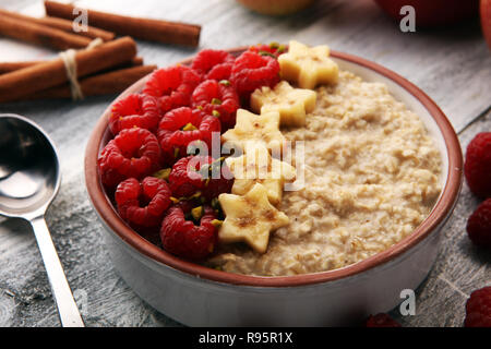 Schüssel Haferbrei Porridge mit Bananen, Himbeeren Kokosnuss und Karamellsauce auf rustikalen Tisch, Warmes und gesundes Essen zum Frühstück. Stockfoto