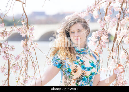 Junge Frau steht zwischen, unter Cherry Blossom, sakura Blumen, Zweige, Baum mit Potomac River im Hintergrund in Washington, DC, mit Sonnenlicht, b Stockfoto