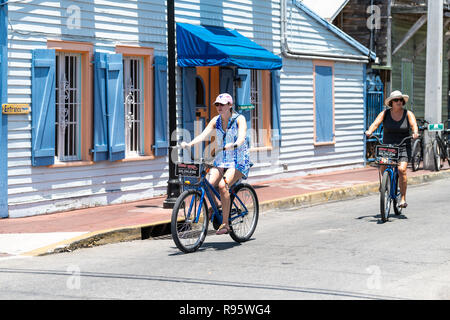 Key West, USA - Mai 1, 2018: Touristen, Menschen, zwei Frauen reiten Reisen Fahrrad, Fahrradverleih mieten, Vermietung auf der Straße Straße in Florida keys Stadt an sonnigen Stockfoto