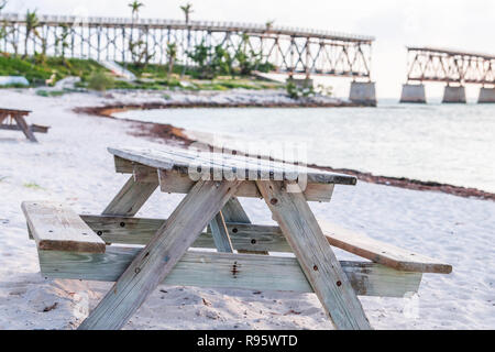 Sand Strand, Picknick Tisch, Sitzbank bei Bahia Honda State Park, Blick auf alte, Rost, Rusty aufgegebenen Rail Road Bridge, Ufer, Küste, Palmen, Himmel bei Sonnenuntergang Stockfoto