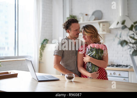 Lassen Sie sich überraschen. Wunderschönes romantisches Paar in der Küche. Junge präsentiert man Blumen zu seinen Geliebten. Das Gefühl von Glück. Stockfoto