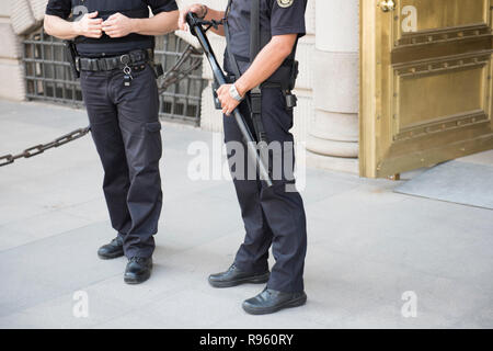 Zwei männliche Polizisten im Einsatz standen vor dem Eingang eines touristischen Ort. Sie werden gesehen, schwarze Uniform mit einer von Ihnen holding Stock in thei Stockfoto