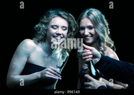 Zwei Mädchen mit Gläsern Champagner in der Hand. Schöne junge Frauen mit Vogue leuchtendes funkeln Gesicht Make-up. Weibliche Weihnachten portrait filmischen Stockfoto