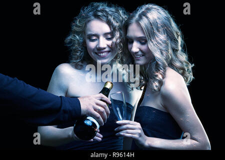 Zwei Mädchen mit Gläsern Champagner in der Hand. Schöne junge Frauen mit Vogue leuchtendes funkeln Gesicht Make-up. Weibliche Weihnachten portrait filmischen Stockfoto