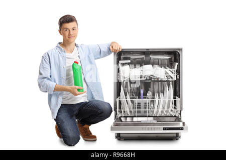 Junge Mann neben einem beladenen Teller Waschmaschine und einem Kunststoff Flasche Reinigungsmittel auf weißem Hintergrund kniend Stockfoto