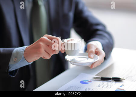 Nahaufnahme eines jungen Geschäftsmann mit einer Tasse Kaffee in der Hand überprüft einige Diagramme Stockfoto