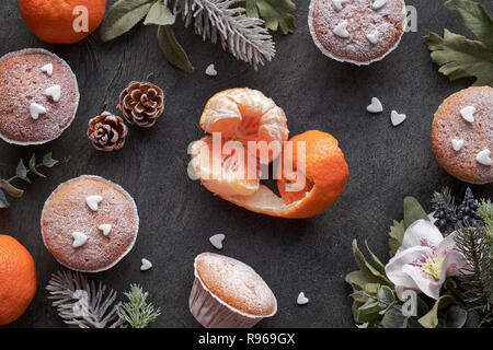 Ansicht von oben in der Tabelle mit satsumas, mit Zucker bestreut Muffins und Christmas Star Cookies auf dunkel strukturierten Hintergrund Stockfoto