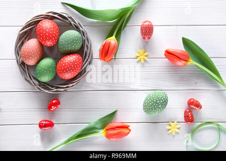 Draufsicht des Lichts Holztisch mit Frühling Dekorationen: rote Tulpen und Ostereier. Frühling oder Ostern Hintergrund Konzept. Stockfoto