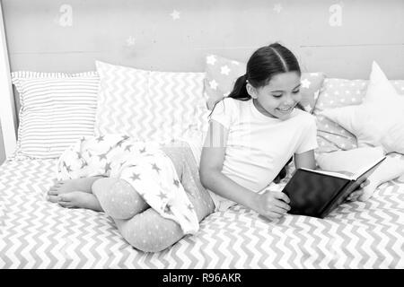 Faszinierende Geschichte. Mädchen legen Bett mit Kissen Buch lesen. Kind vorbereiten, ins Bett zu gehen. Zeit für den Abend faszinierende Geschichte. Mädchen Junge lange Haare niedliche Schlafanzug entspannen und faszinierende Geschichte Buch lesen. Stockfoto