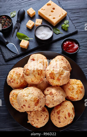 Gougeres, Käse Puffs Kugeln auf schwarzem Teller. Traditionelle französische Käse choux Brötchen, Käse und Tomaten Soße auf einer schwarzen Holztisch, vertikale Ansicht fr Stockfoto