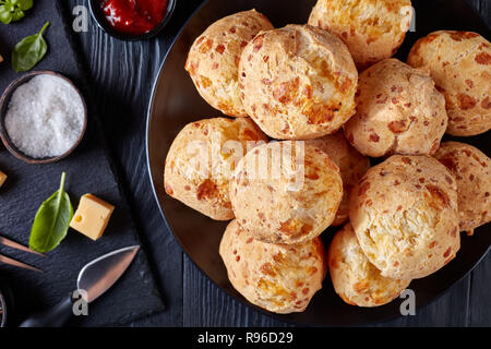 Ansicht von oben von Gougeres, Käse Puffs Kugeln auf schwarzem Teller. Traditionelle französische Käse choux Brötchen, Käse und Tomaten Soße auf einer schwarzen Holztisch, Stockfoto