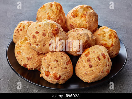 Köstlich knusprige Gougeres, Käse Puffs Kugeln auf schwarzem Teller. Traditionelle französische Käse choux Brötchen auf einer konkreten Tabelle, Ansicht von oben, close-up Stockfoto